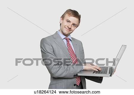 Handsome young businessman using laptop over colored background View Large Photo Image Picture - Handsome young businessman using laptop over colored background. Fotosearch