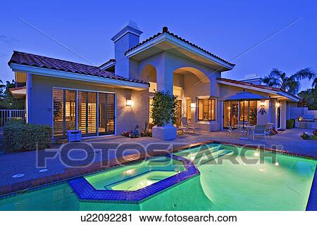 Stock Image - Illuminated swimming pool with Jacuzzi in front of luxury mansion. Fotosearch