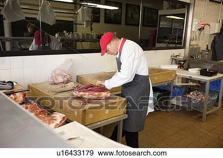 Stock Photo - Male butcher slicing beefsteak in store. Fotosearch
