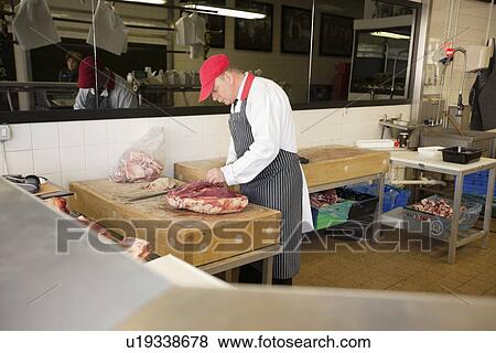 Stock Photo - Mature man cutting beefsteak in butcher shop. Fotosearch