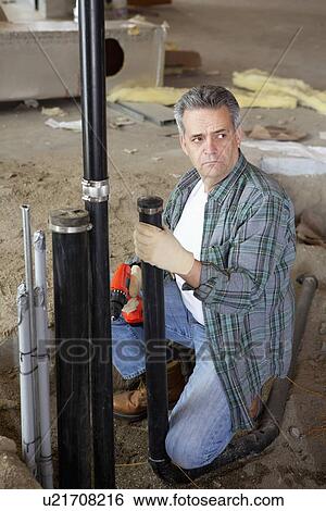 Stock Photograph - Mature man looking away while holding pipe and drill. Fotosearch