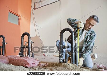 Stock Photograph - Mature man measuring pipe with tape at construction site. Fotosearch