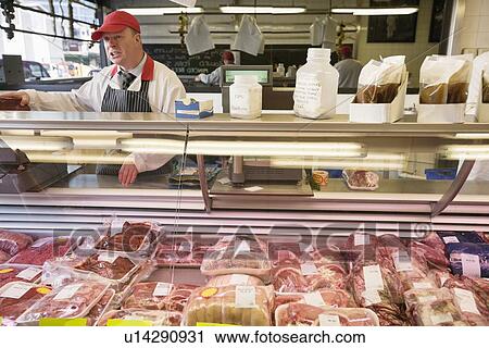 Meat in display case with butcher standing in background View Large Photo Image Stock Image - Meat in display case with butcher standing in background. Fotosearch