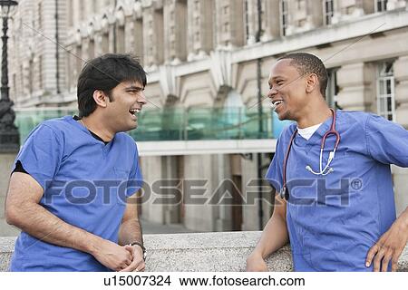 Picture - Multi ethnic doctors laughing over something with building in background. Fotosearch