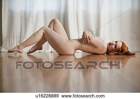 Naked Young Woman Lying On Wooden Floor At Home Stock Photo
