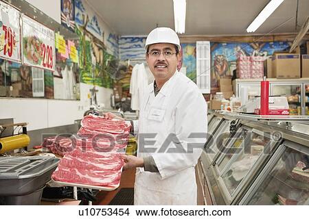 Picture - Portrait of a butcher holding meat tray in shop. Fotosearch