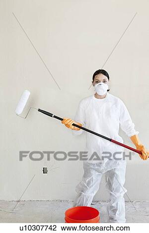 Stock Image - Portrait of a female worker in protective workwear holding a paint roller. Fotosearch
