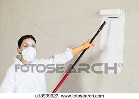 Stock Image - Portrait of a female worker in protective workwear painting wall. Fotosearch