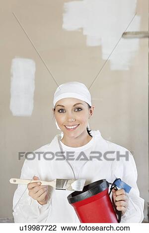 Stock Image - Portrait of a happy female worker holding a paint brush and bucket. Fotosearch