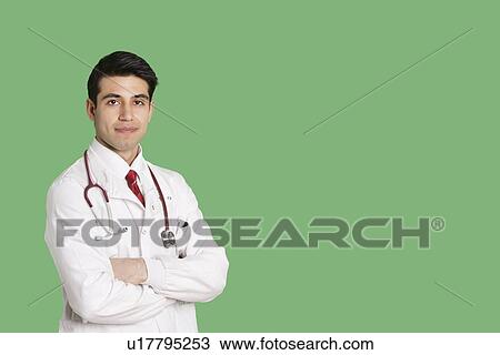 Stock Image - Portrait of a male healthcare professional standing with arms crossed over green background. Fotosearch