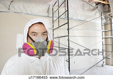 Stock Image - Portrait of a male worker wearing dust mask with scaffold in background. Fotosearch
