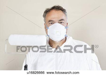 Stock Photograph - Portrait of a manual worker wearing protective mask and holding a paint roller. Fotosearch