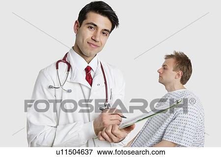 Stock Photo - Portrait of an Indian doctor writing prescription with patient sitting behind. Fotosearch