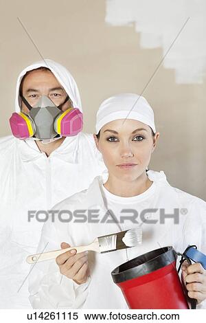 Stock Photography - Portrait of female worker holding paint tools with male worker standing behind. Fotosearch