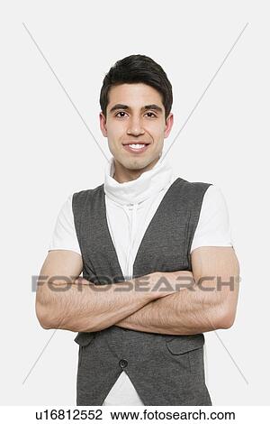 Stock Image - Portrait of handsome young man with arms crossed over colored background. Fotosearch