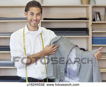 Portrait of handsome young tailor holding custom made suit View Large Photo Image Stock Photo - Portrait of handsome young tailor holding custom made suit. Fotosearch