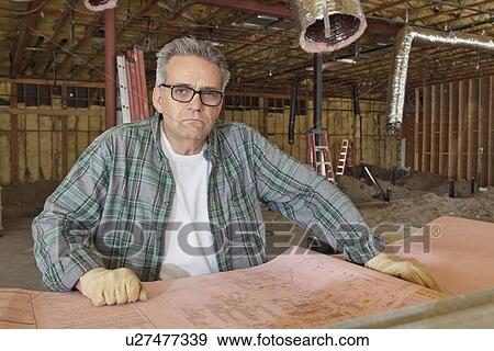 Stock Photo - Portrait of mature architect wearing glasses with blueprint at construction site. Fotosearch