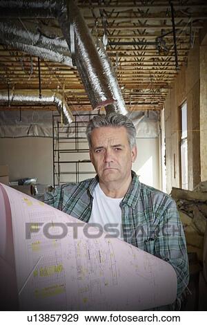 Stock Photo - Portrait of mature architect with blueprint at construction site. Fotosearch