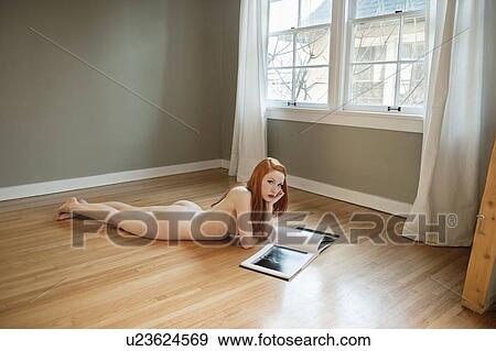Portrait Of Naked Woman Lying On Wooden Floor Reading Book Stock