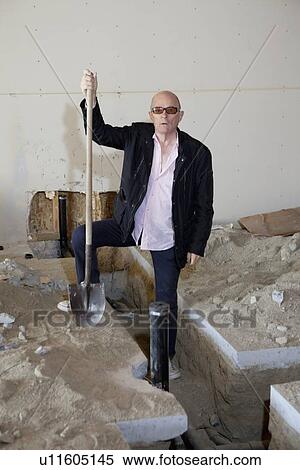 Stock Photography - Portrait of senior owner of property standing with shovel at construction site. Fotosearch