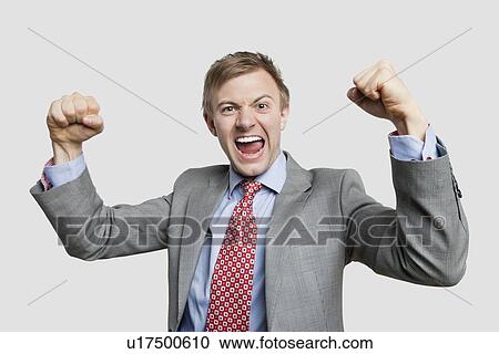 Stock Image - Portrait of young businessman screaming while clenching fist over light gray background. Fotosearch