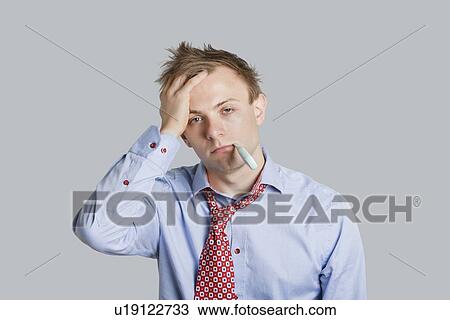 Stock Image - Portrait of young man in formal wear with thermometer in mouth over colored background. Fotosearch