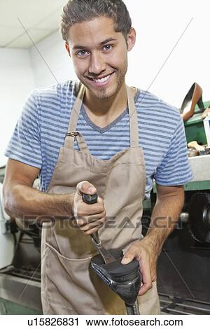 Stock Image - Portrait of young shoemaker working on shoe sole with hammer in workshop. Fotosearch