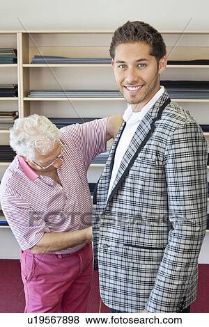 Stock Photo - Senior tailor measuring young customer for making suit. Fotosearch