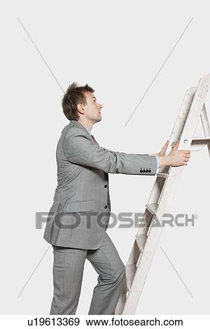 Side view of young businessman climbing ladder over colored background View Large Photo Image Stock Photo - Side view of young businessman climbing ladder over colored background. Fotosearch