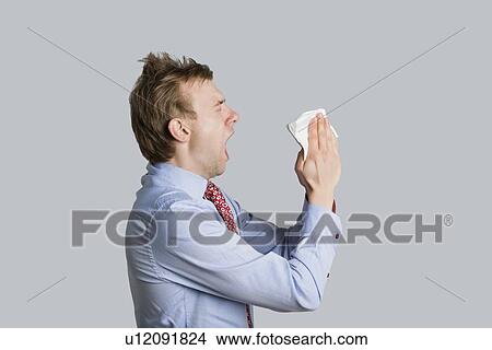 Picture - Side view of young man sneezing while trying to cover mouth over colored background. Fotosearch