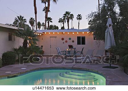 Stock Image - Swimming pool with chaise lounge in evening lights. Fotosearch