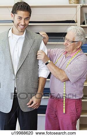 Stock Image - Tailor assisting young customer in custom made suit. Fotosearch