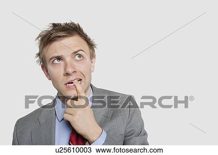 Thoughtful young businessman biting finger while looking up over colored background View Large Photo Image Stock Image - Thoughtful young businessman biting finger while looking up over colored background. Fotosearch
