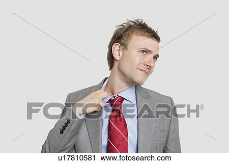 Stock Image - Tired young businessman loosening tie over colored background. Fotosearch