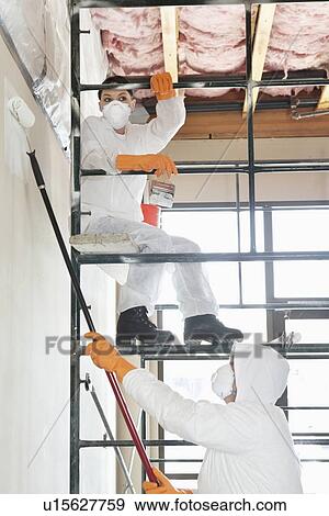 Stock Photo - Two construction workers on scaffold painting a room. Fotosearch
