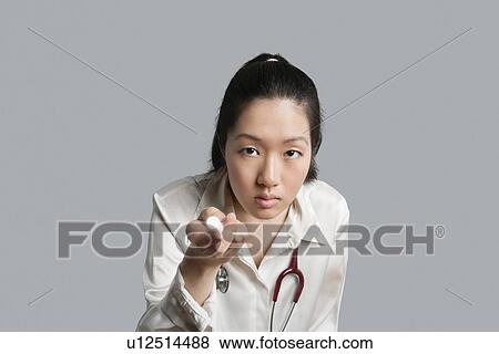 Stock Photo - Young Asian female doctor holding a flashlight over gray background. Fotosearch