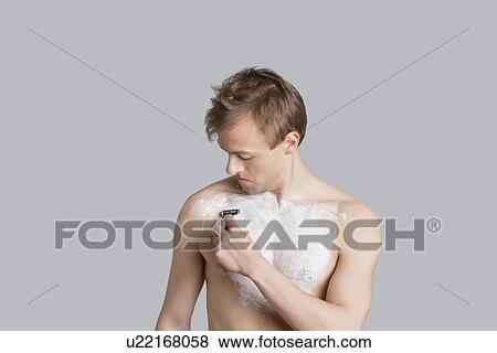 Young man shaving chest with razor over colored background View Large Photo Image Stock Photo - Young man shaving chest with razor over colored background. Fotosearch