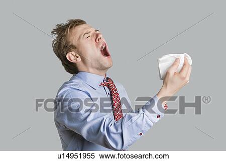 Young man sneezing with open mouth and handkerchief over colored background View Large Photo Image Stock Photography - Young man sneezing with open mouth and handkerchief over colored background. Fotosearch