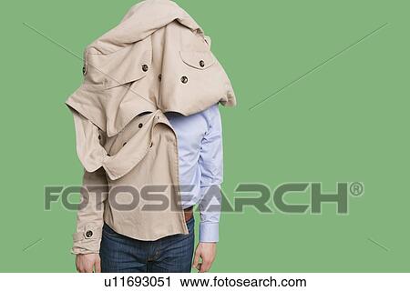 Stock Image - Young man standing with jacket over head over colored background. Fotosearch