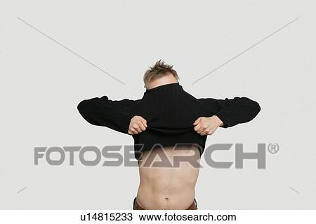 Stock Image - Young man struggling to pull down t-shirt over colored background. Fotosearch