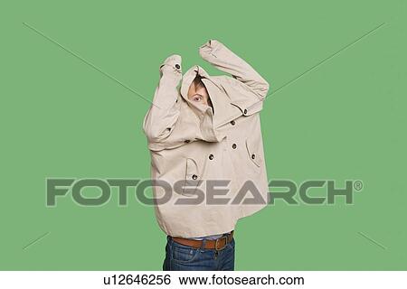 Stock Photograph - Young man wearing jacket while looking from jacket over colored background. Fotosearch