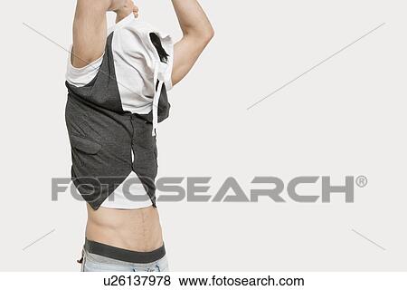 Young man with arms raised struggling to dress up over colored background View Large Photo Image Stock Photo - Young man with arms raised struggling to dress up over colored background. Fotosearch