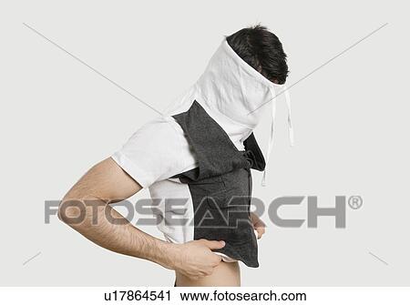 Stock Image - Young man with covered face while wearing t-shirt over colored background. Fotosearch