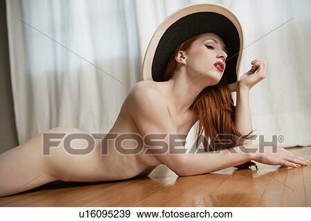 Young Woman Lying Naked On Wooden Floor With A Hat Stock Photo