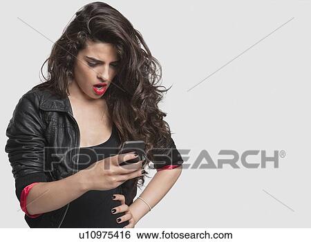 Amazed young female using cell phone against gray background View Large Photo Image Stock Photograph - Amazed young female using cell phone against gray background. Fotosearch