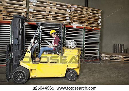 Stock Photography - Asian female industrial worker looking at clipboard while sitting in a forklift truck. Fotosearch