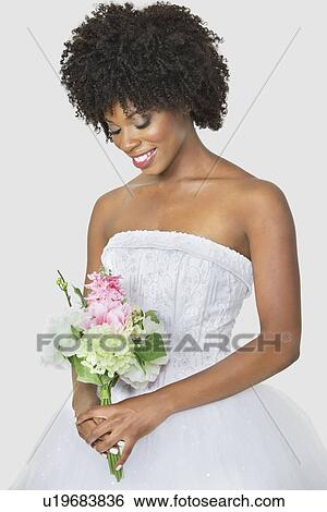 Stock Photograph - Beautiful African American bride holding bouquet over gray background. Fotosearch