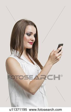 Stock Photography - Beautiful young woman using cell phone against gray background. Fotosearch