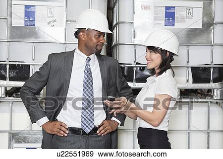 Stock Photo - Businesswoman showing cell phone to male colleague. Fotosearch