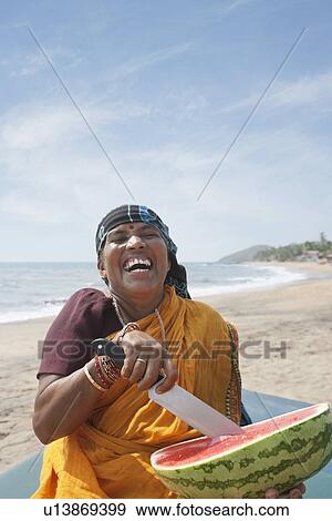 Stock Photo - Cheerfulness mature Indian woman cutting watermelon at Vagator Beach, Goa, India. Fotosearch